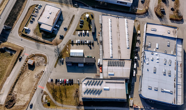 Luftaufnahme von der Newo Sonnen- und Insektenschutz GmbH mit mehreren Gebäuden und parkenden Autos. Man sieht eine Kreuzung und Straßen, die das Gebiet umgeben. Luftbild von der Newo Sonnen- und Insektenschutz GmbH mit Gebäuden und parkenden Autos.