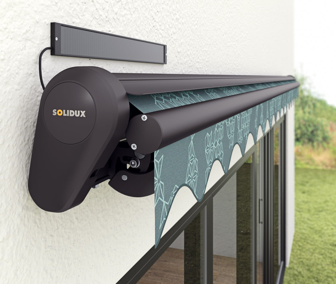 Kassettenmarkise mit SOLIDUX-Antrieb und Solarpanel an der Hauswand, Markisentuch ausgefahren vor Glasfront.